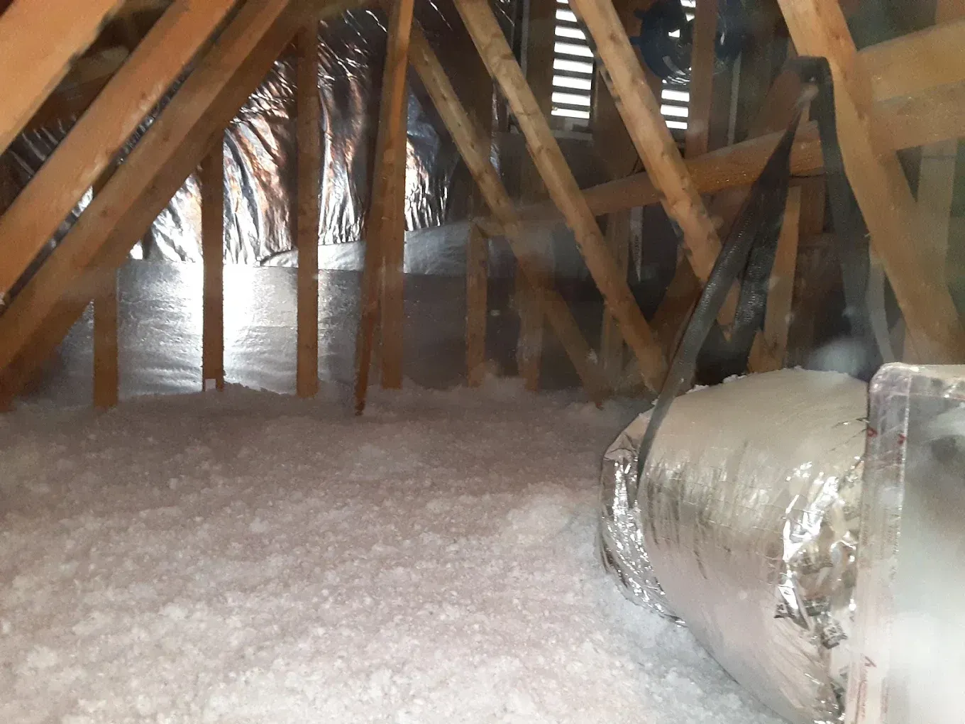 An attic with white insulation and a metal pipe