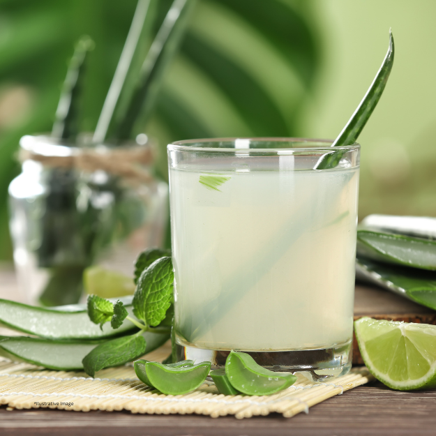 A glass of aloe vera juice is on a table next to aloe vera leaves and limes.