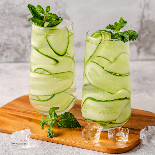 Two glasses of cucumber juice with mint leaves on a wooden cutting board.