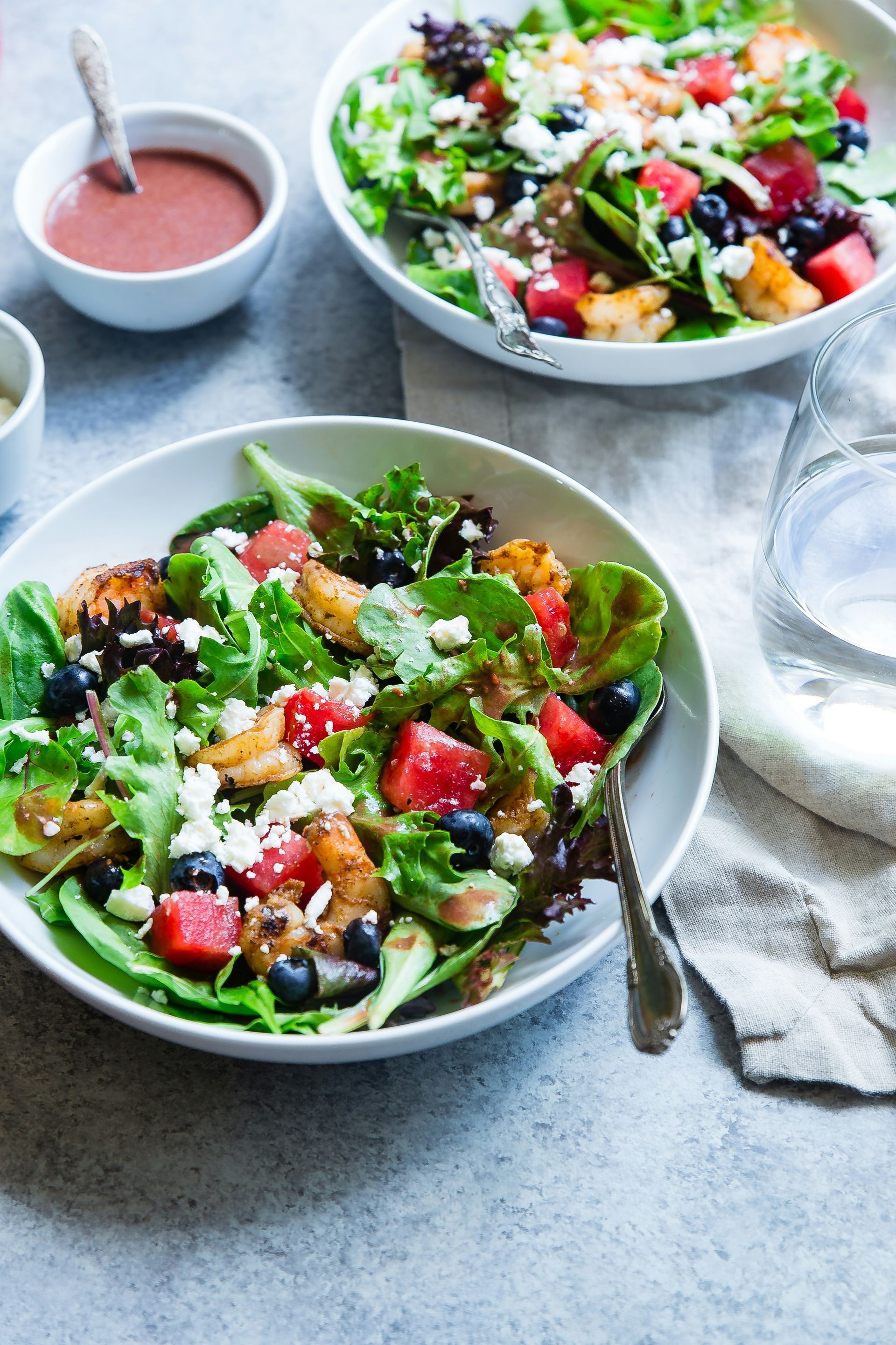 Two bowls of salad with watermelon , blueberries and feta cheese on a table.