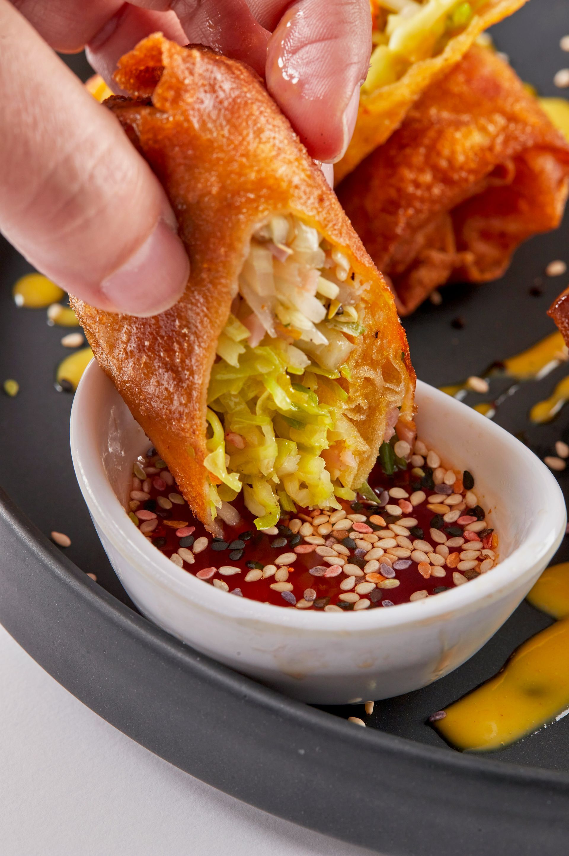 A person is dipping an egg roll in a bowl of dipping sauce.