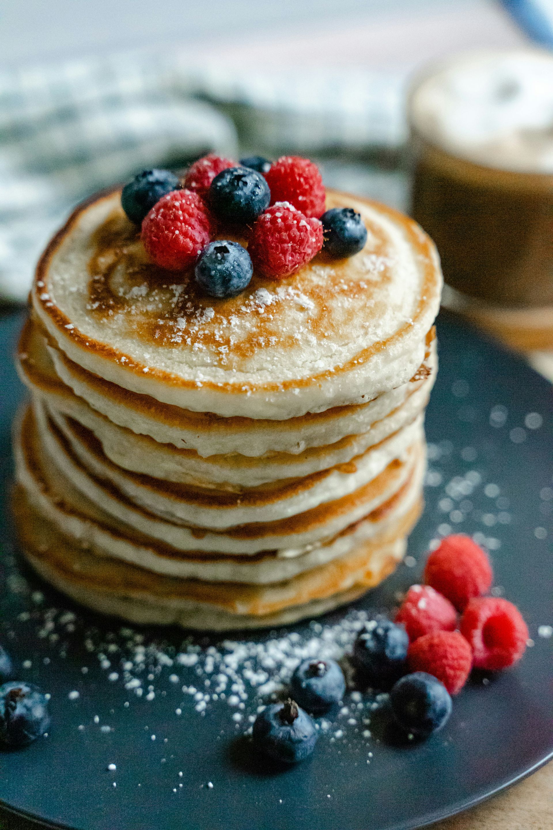 A stack of pancakes with raspberries and blueberries on top on a black plate.