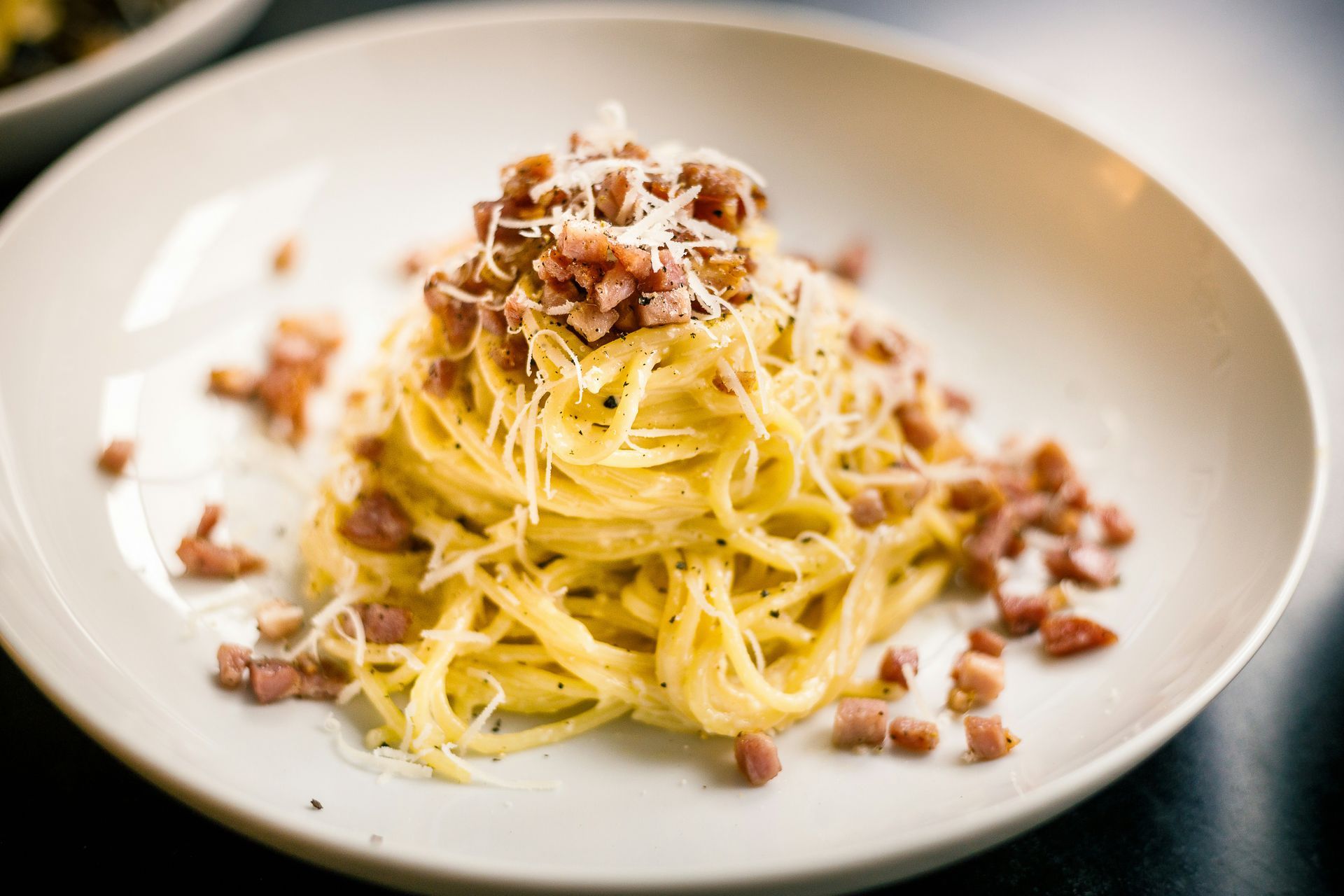 A white plate topped with spaghetti and bacon on a table.