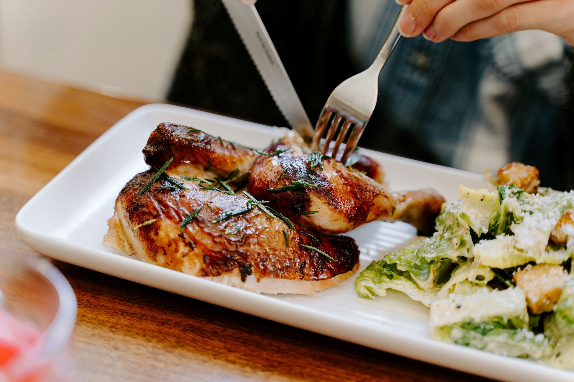 A person is cutting a piece of chicken on a plate with a fork.