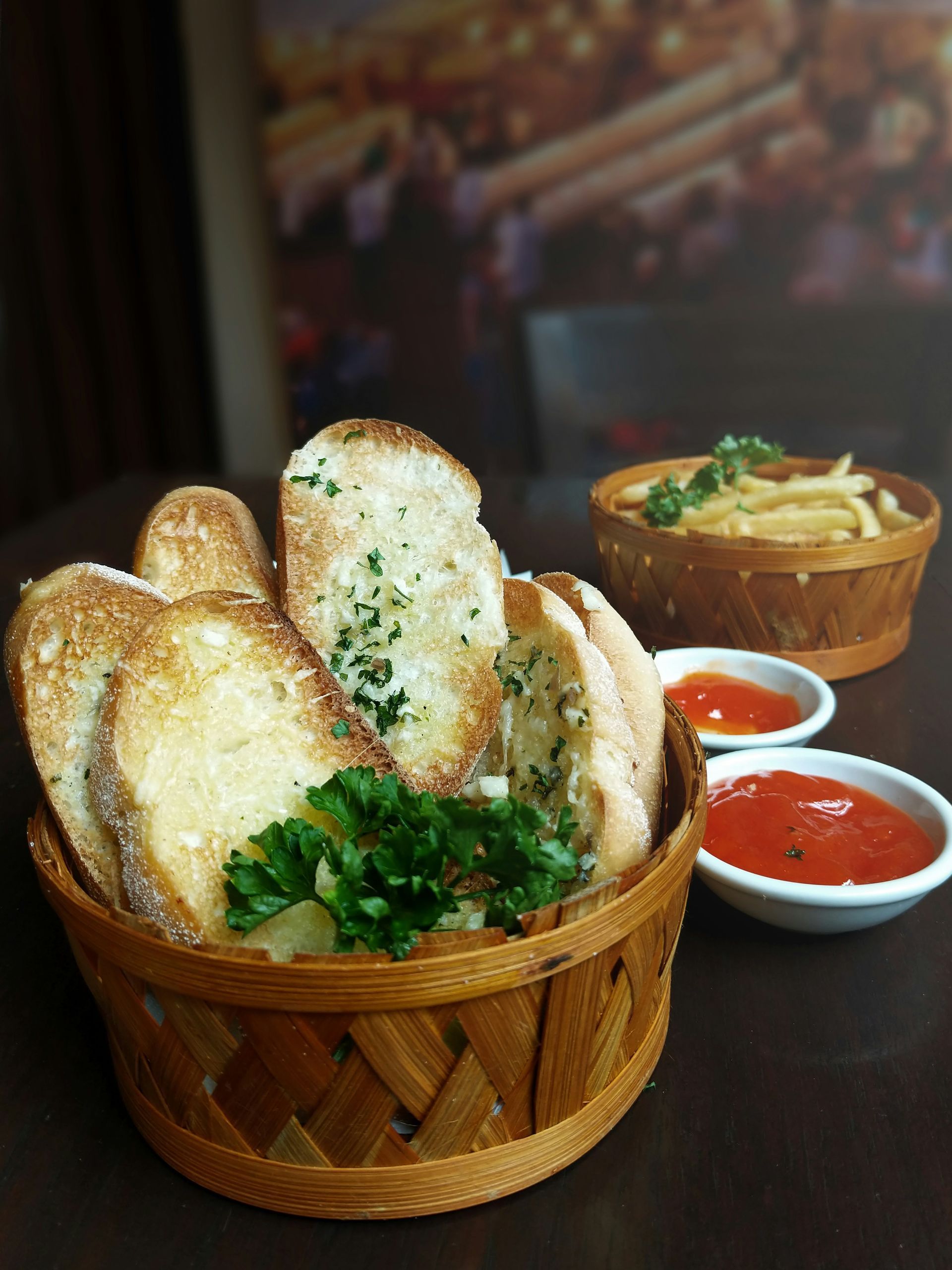 A basket of garlic bread is sitting on a table next to a bowl of french fries.