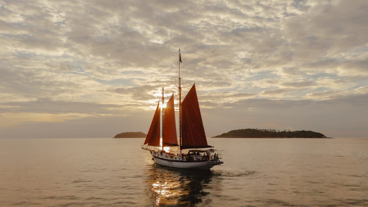 A sailboat with red sails is floating on top of a body of water.