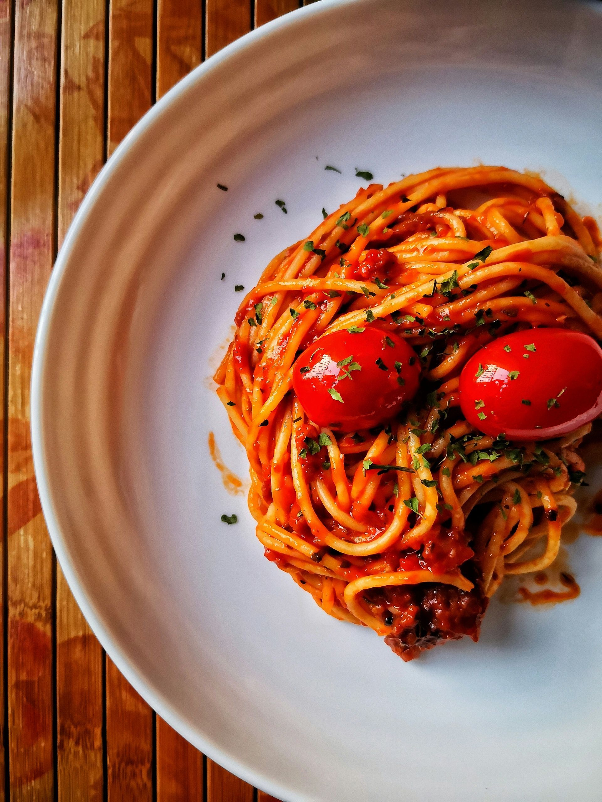 A white plate topped with spaghetti and tomatoes on a wooden table