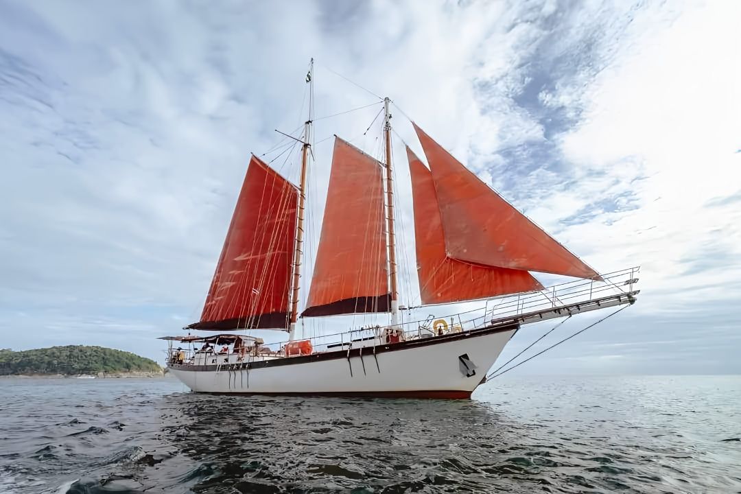 A large sailboat with red sails is floating on top of a body of water in Thailand.