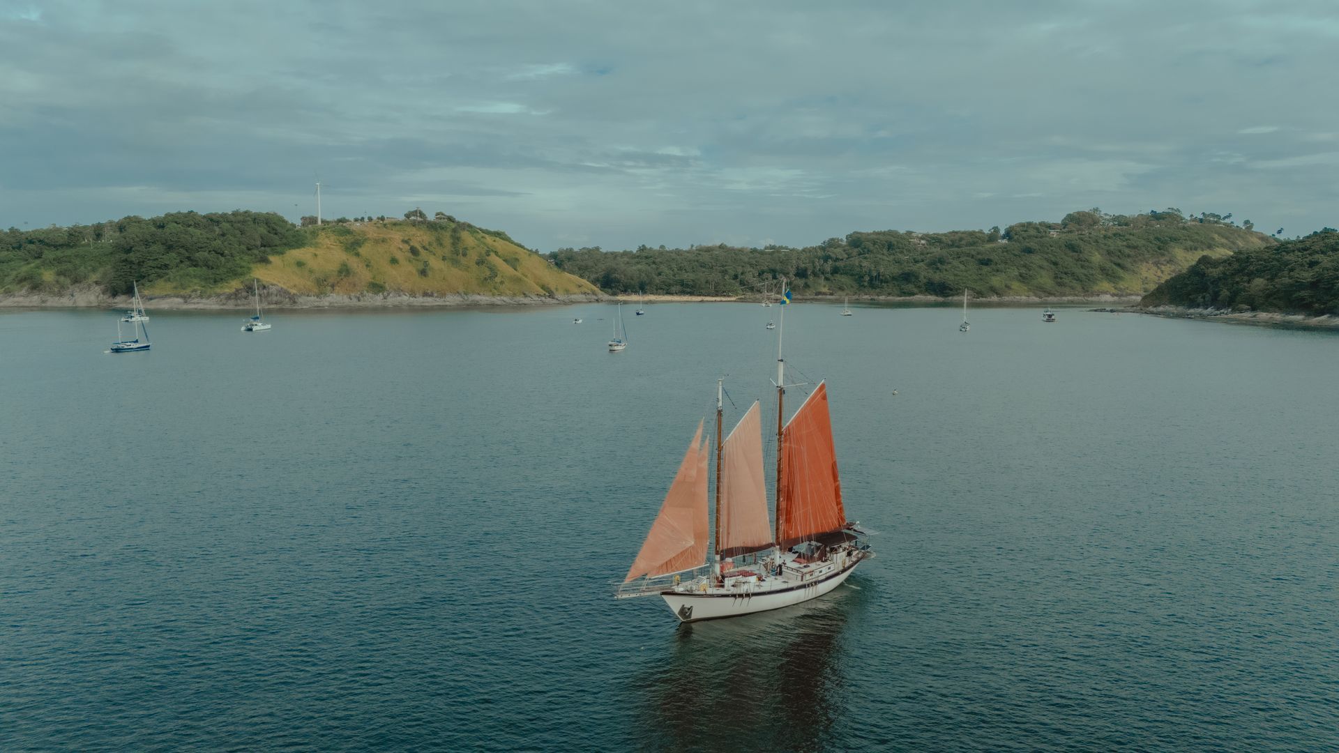 A sailboat - schooner - with red sails is floating on top of a body of water.