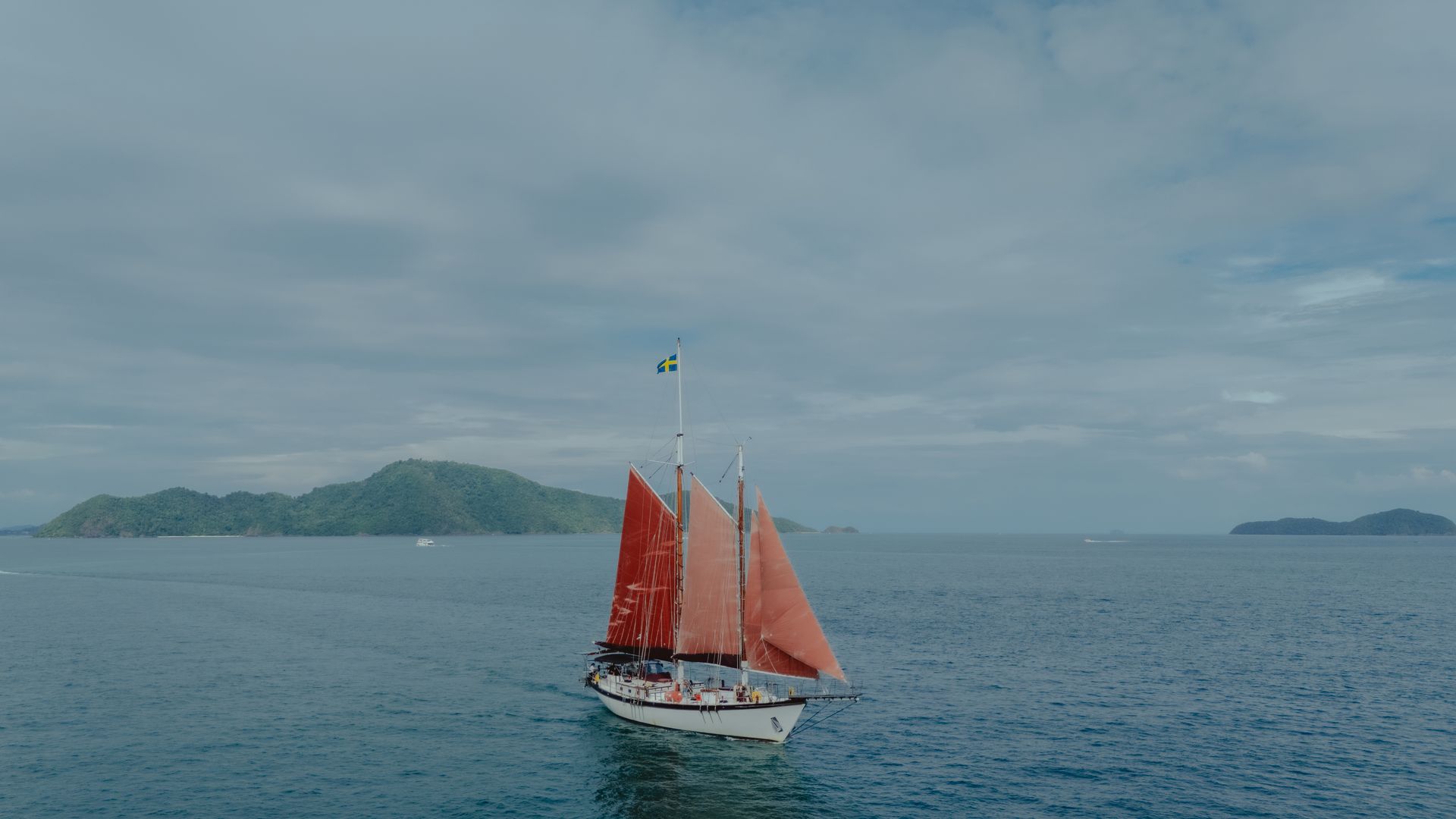 A sailboat - schooner - with red sails is floating on top of a body of water.