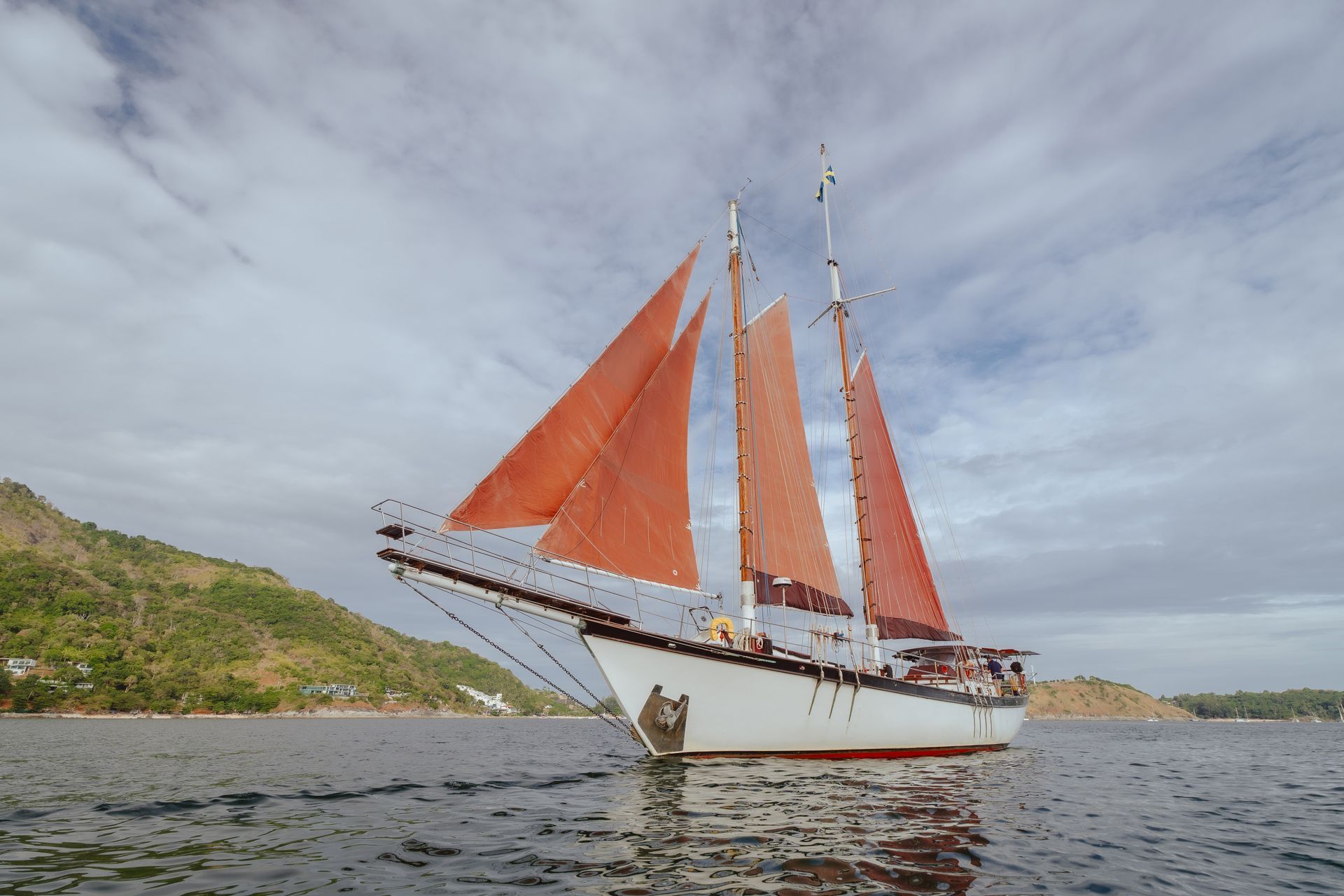 A sailboat - schooner - with red sails is floating on top of a body of water.