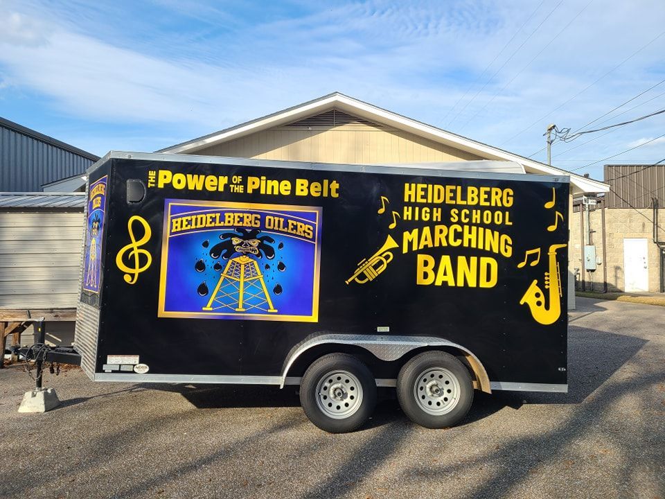 A black Heidelberg High School marching band equipment trailer with gold lettering and musical instrument graphics.