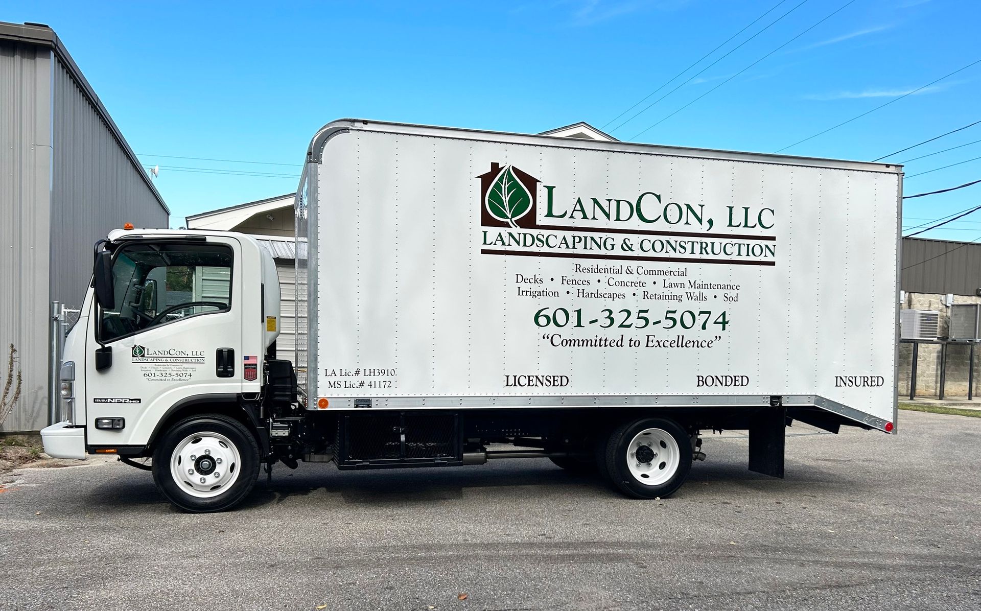 A white LandCon, LLC landscaping and construction box truck parked on a gravel lot in front of a metal building.