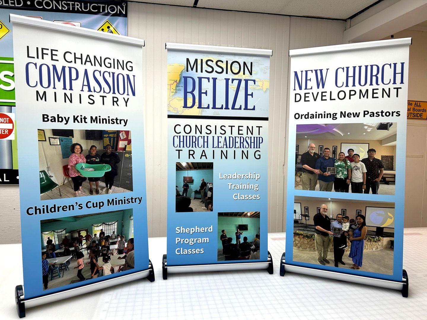 Three retractable banners showcasing ministries: Life Changing Compassion, Mission Belize, and New Church Development.