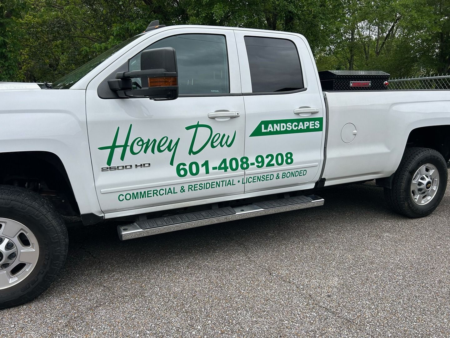 A white crew cab pickup truck parked on gravel, branded with green text reading 