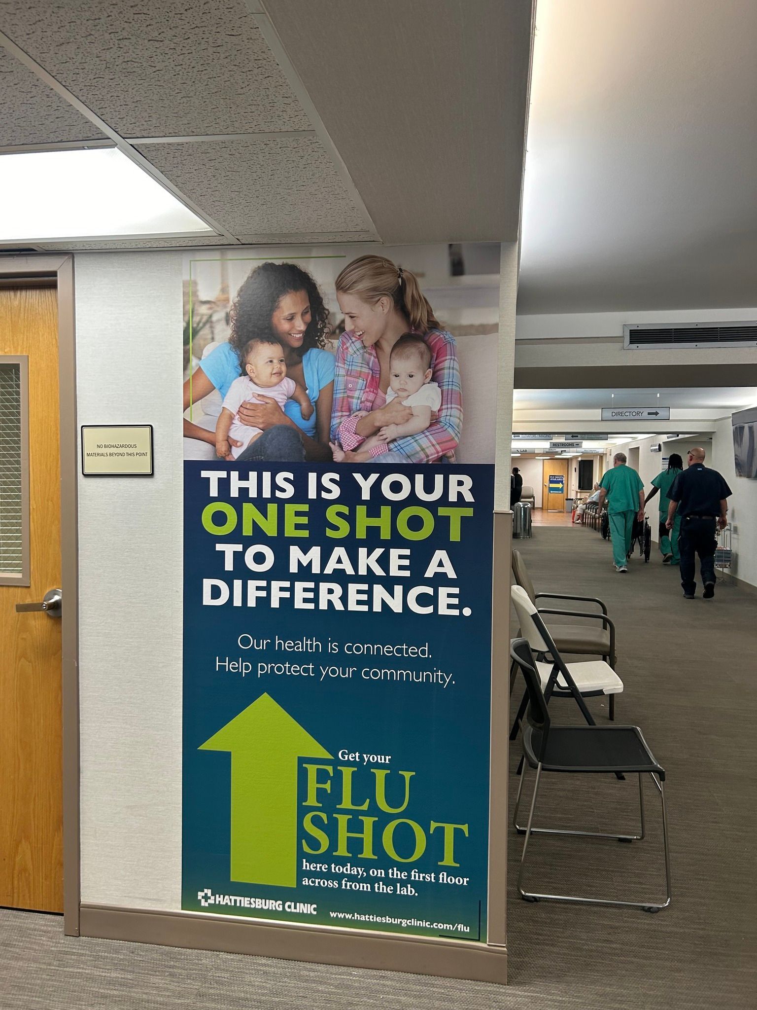 A hallway sign featuring two people holding babies, promoting a flu shot with the text 