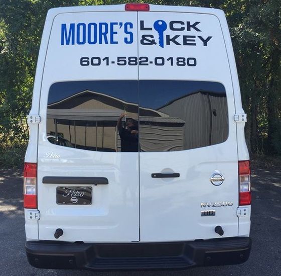 The rear view of a white Moore's Lock & Key van with phone number 601-582-0180 parked outside.