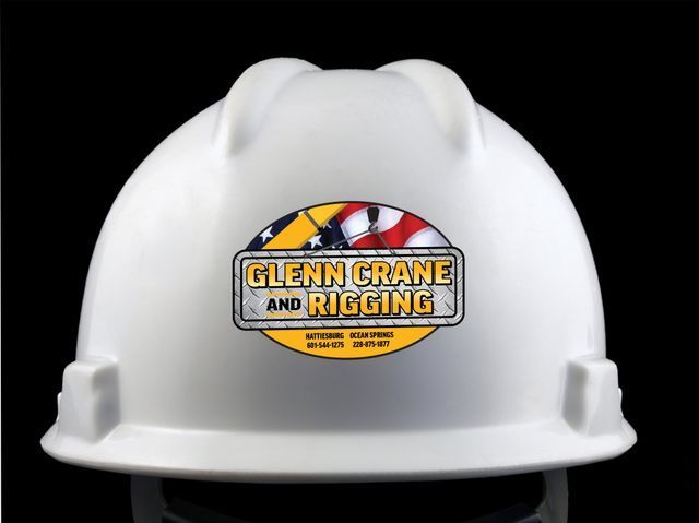 White hard hat featuring a Glenn Crane and Rigging company logo with American flag elements on a black background.