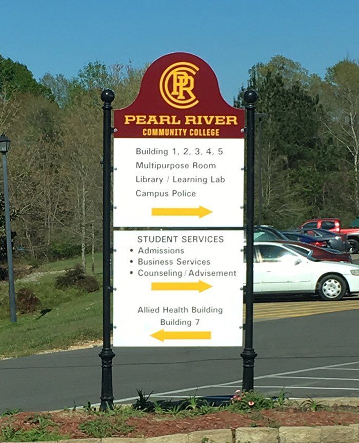 A Pearl River Community College campus directional sign featuring white text and yellow arrows on a burgundy and white background.