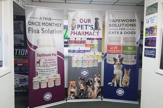 Three vertical display banners in a shop advertising pet pharmacy products for fleas and tapeworms for cats and dogs.