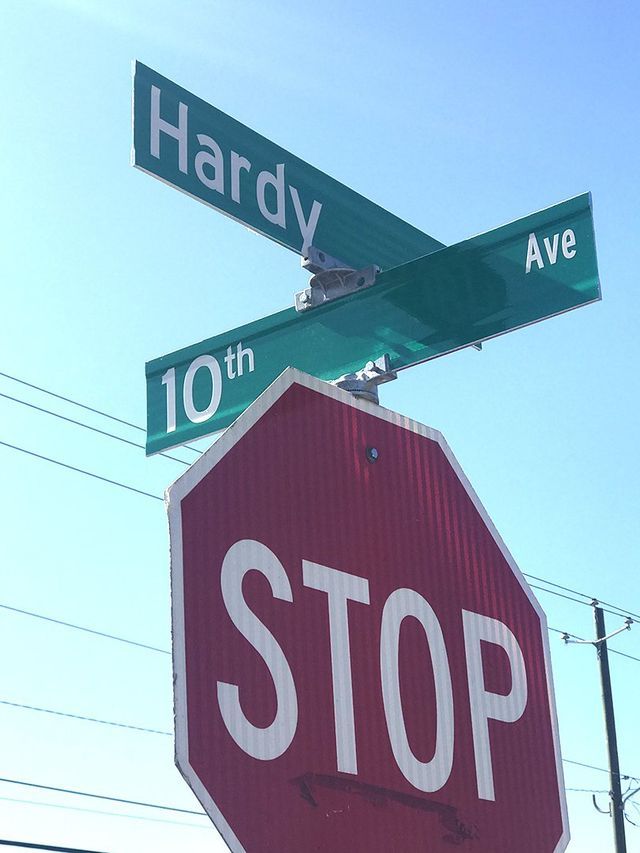 A red stop sign sits beneath green street signs for Hardy Ave and 10th Ave against a bright blue sky.