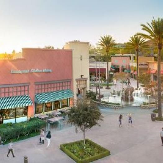 Outdoor shopping center with restaurants, walkways, and palm trees in sunlight.
