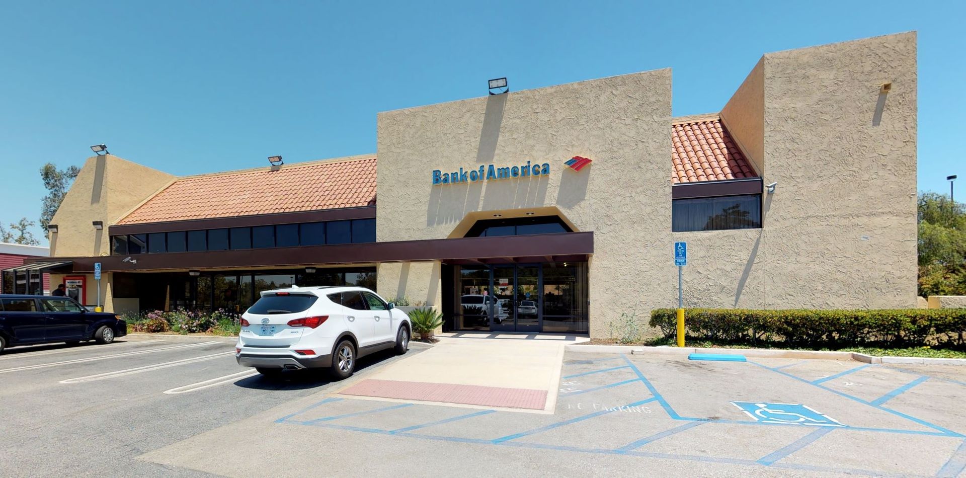 Bank of America building with white SUV parked in front. Blue sky.