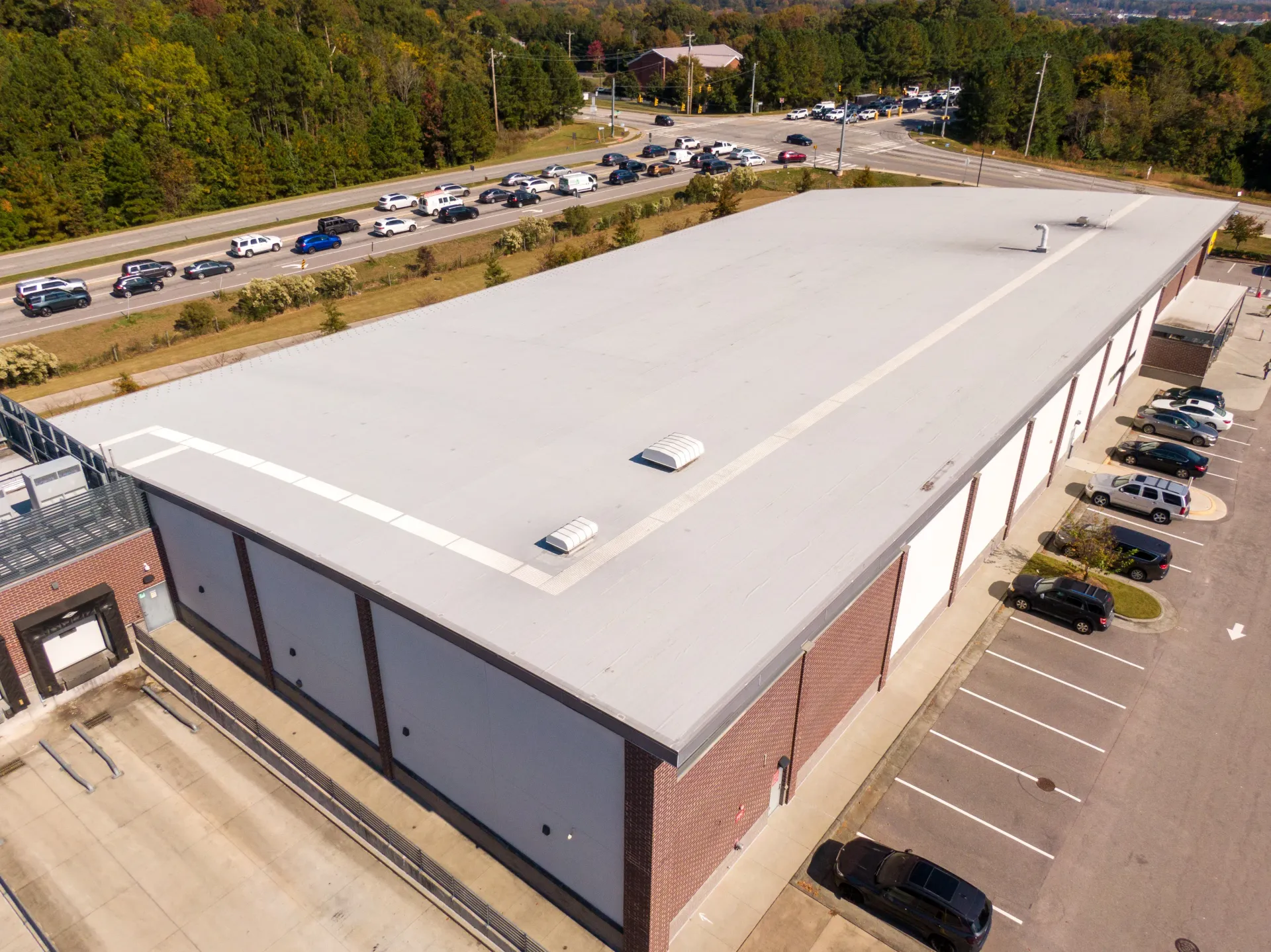 Aerial view of a long, flat-roofed building with a brick facade and cars parked nearby.