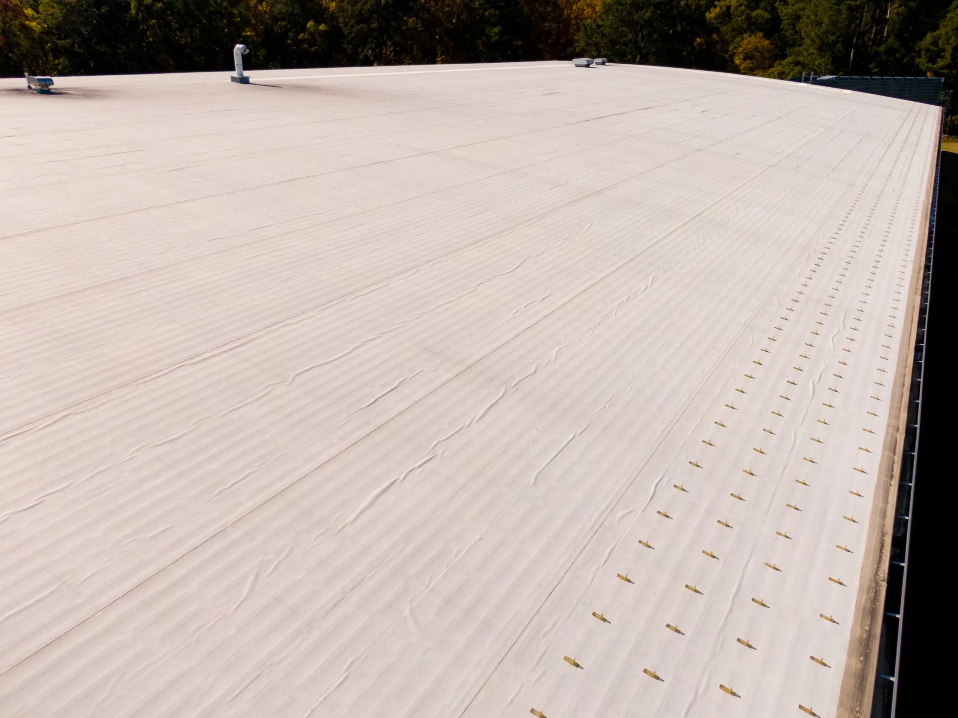 Large, flat, off-white commercial roof with vents and slight undulations.