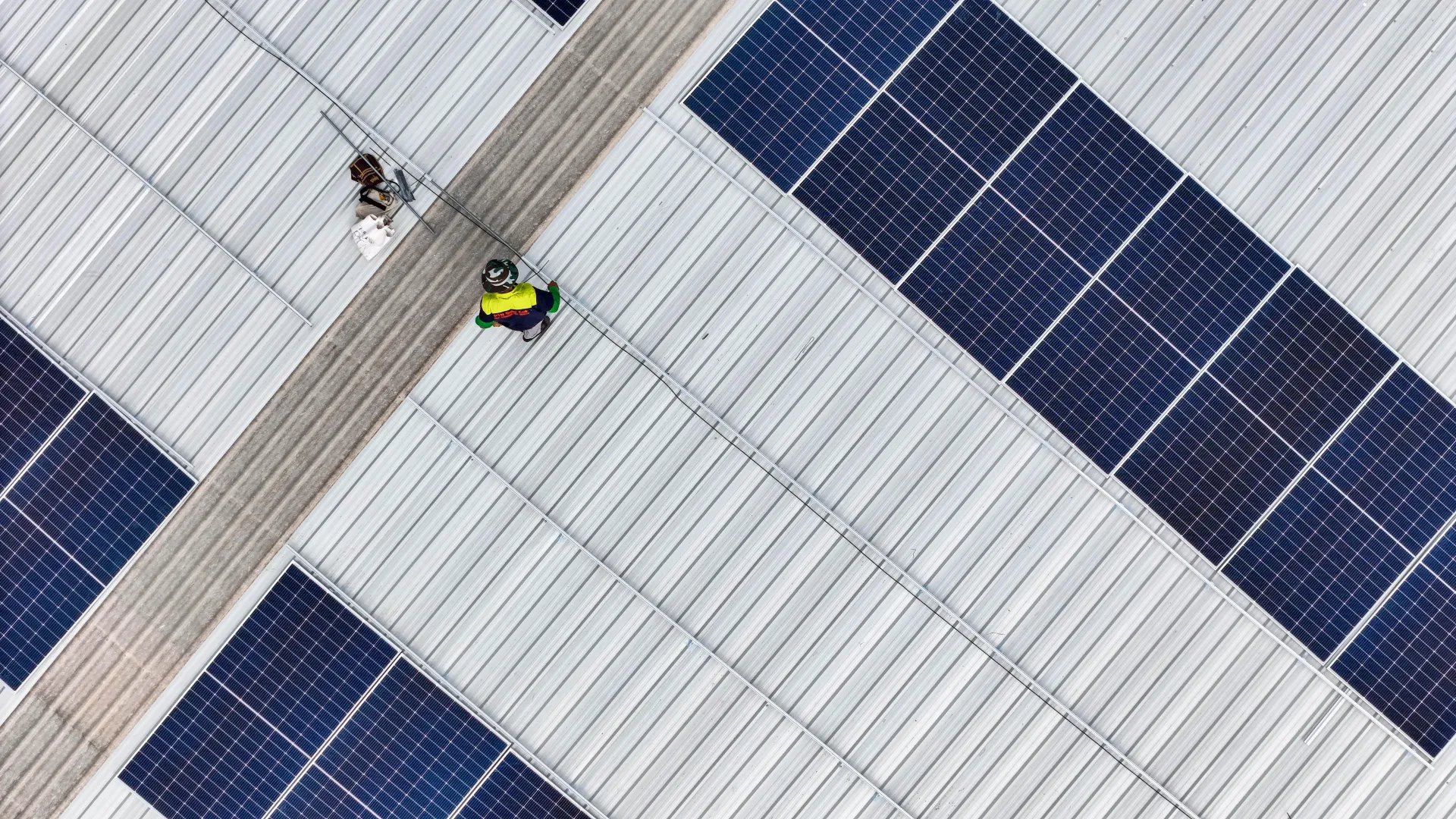 Workers on a rooftop solar panel array, with blue panels and connecting walkways.