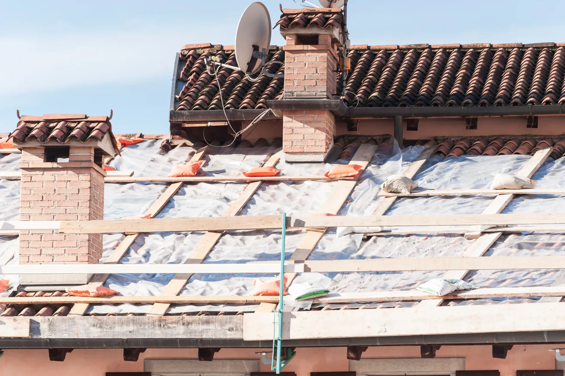 Roof partially under construction with visible wooden beams, insulation, and red brick chimneys.