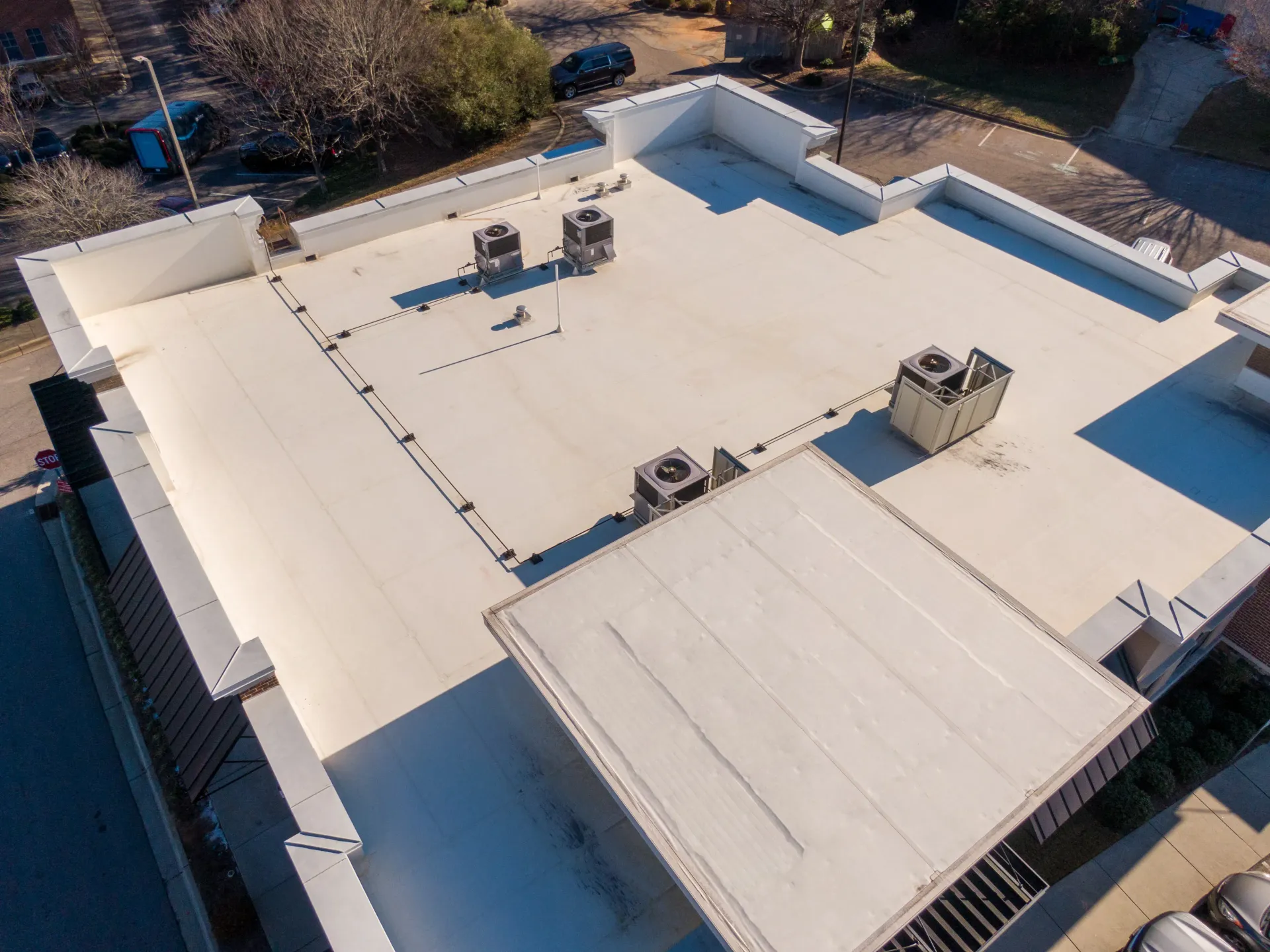 Aerial view of a flat white roof with multiple HVAC units and perimeter walls.