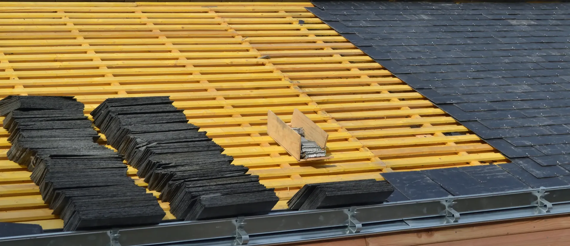 Roof under construction: yellow latticework with stacks of black shingles and partially completed dark roof.