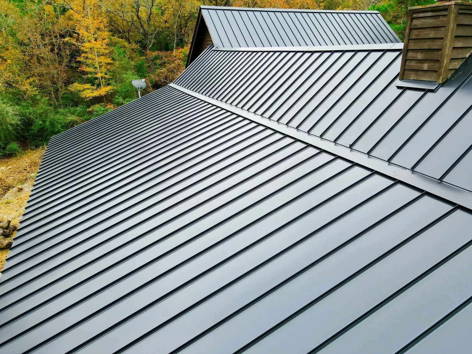 Dark gray metal roof with vertical ridges on a house, outdoor setting.