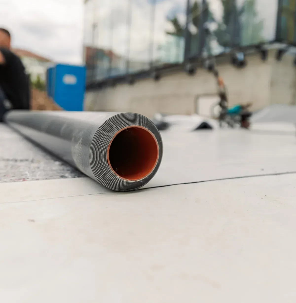 Close-up of a black pipe with a patterned edge and orange interior, lying on a white surface, construction site.