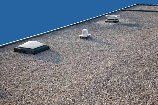 Flat gravel roof with three vents against a blue sky.