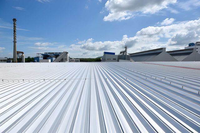 White corrugated metal roof under a blue sky, factory buildings in the background.