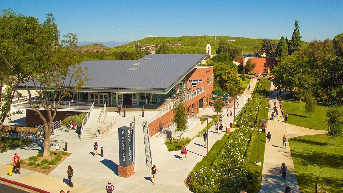 College campus with a brick building and a path lined with flowers, people walking.