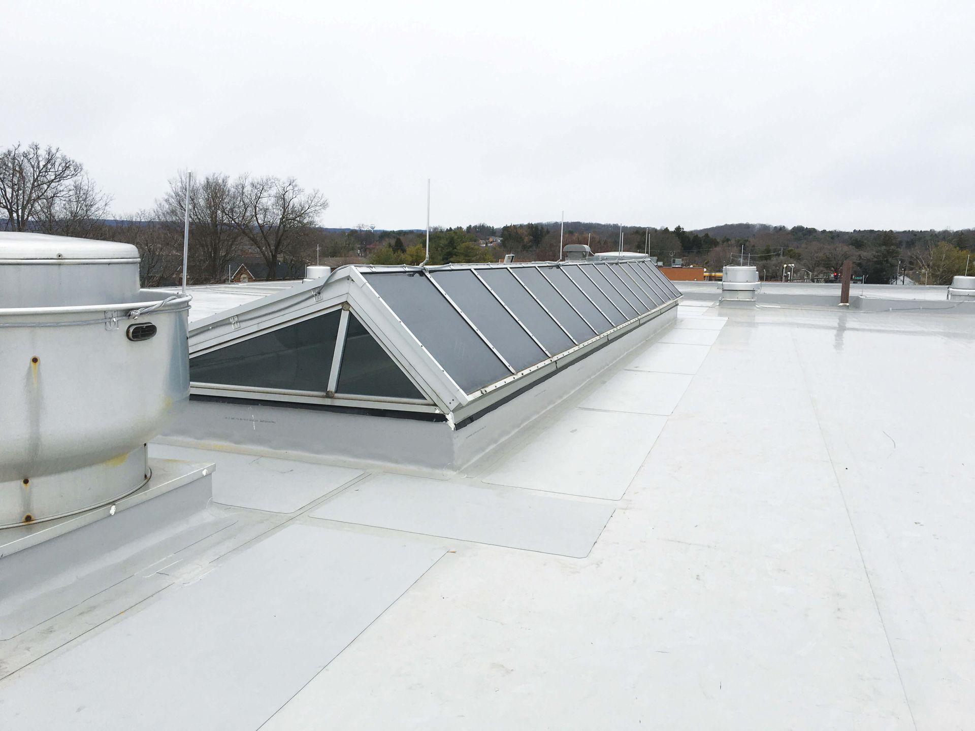 White commercial roof with a long skylight, metal vent, and a cloudy sky.