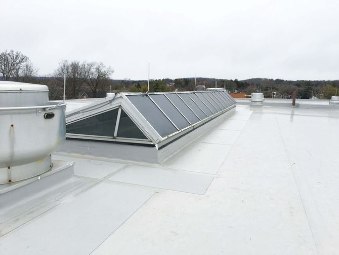 White commercial roof with a long skylight, metal vent, and a cloudy sky.