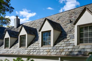 Gray slate roof with several dormer windows under a blue sky.