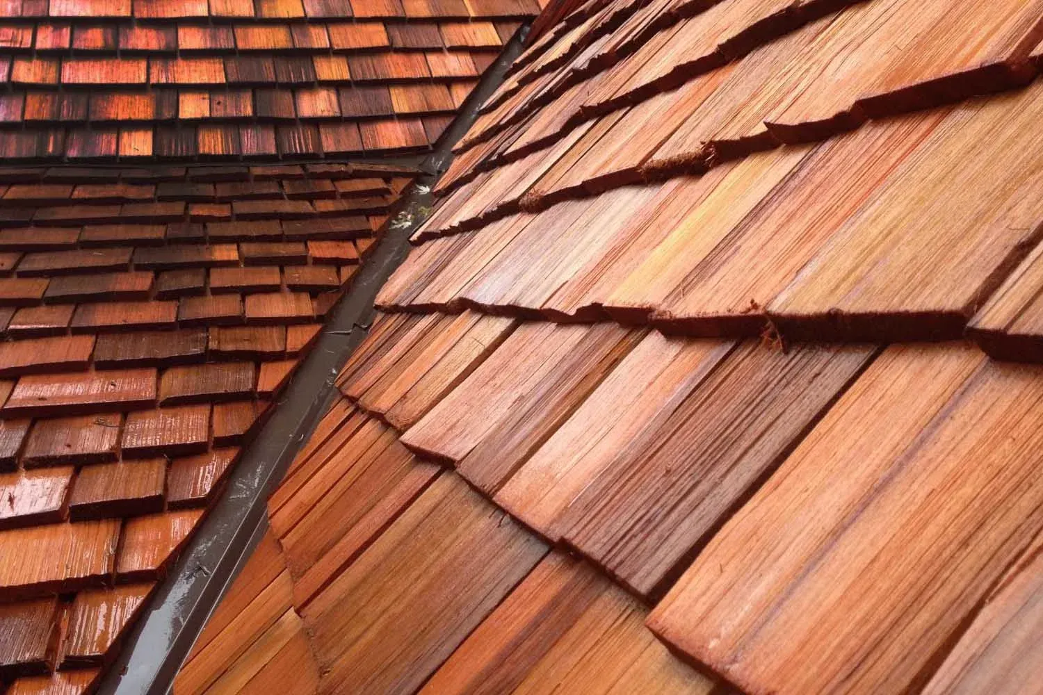 Close-up of a cedar shake roof with varying shades of brown and a dark metal gutter.