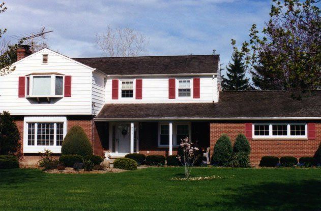 New Windows with red shutters installed in a white house with brown roofing Grand Island, NY