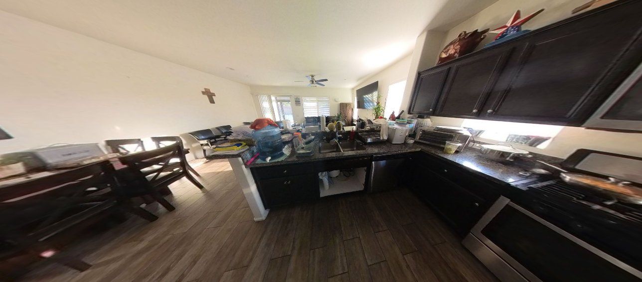 A wide-angle shot of a kitchen with dark cabinets, stainless steel appliances, and a wooden table in the foreground.