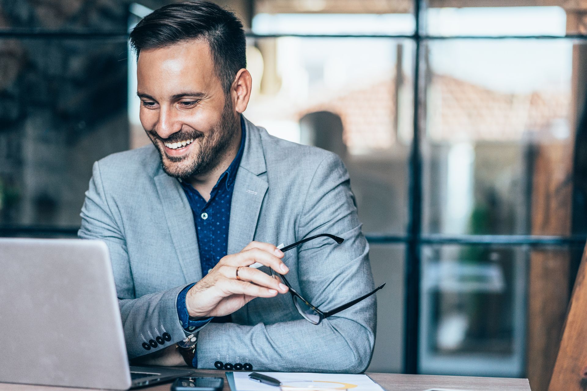 A man in a suit is sitting at a desk using a laptop computer.