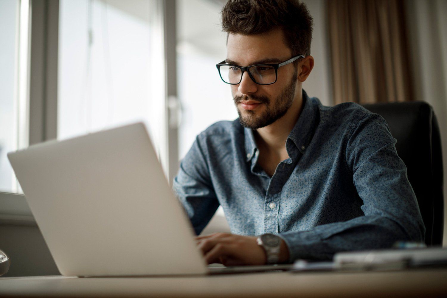 A man is sitting at a desk using a laptop computer.