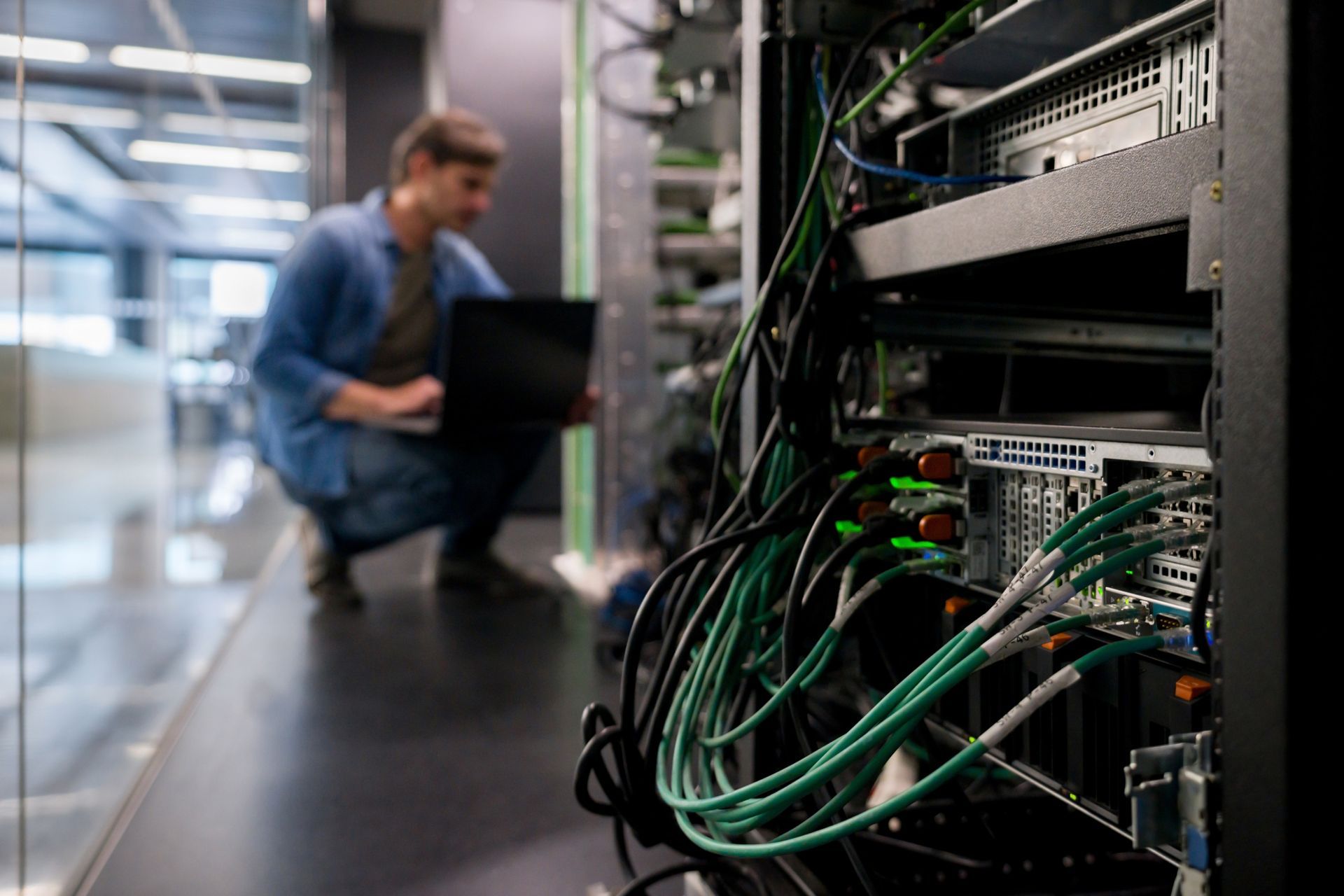 A man is working on a laptop in a server room.