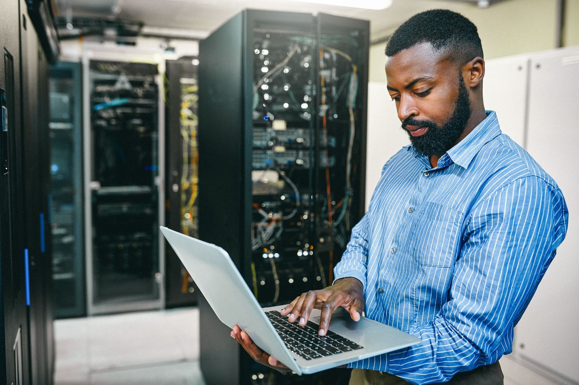 A man is using a laptop computer in a server room.