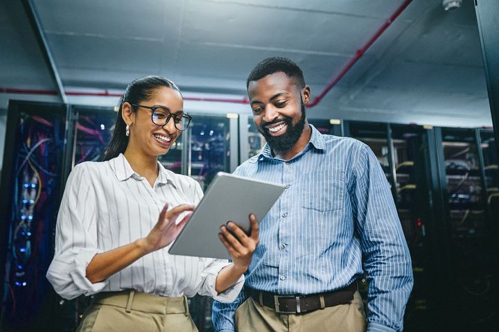 A man and a woman are looking at a tablet in a server room.