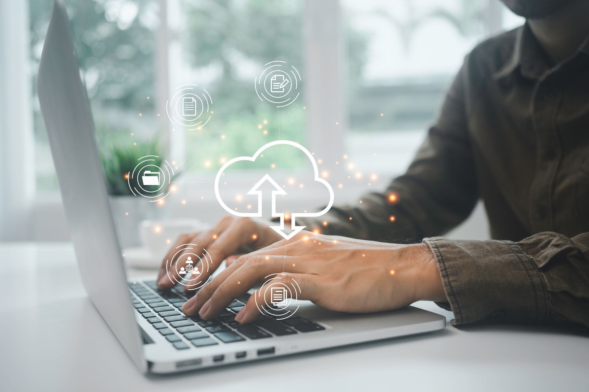 A man is typing on a laptop computer with a cloud icon coming out of it.